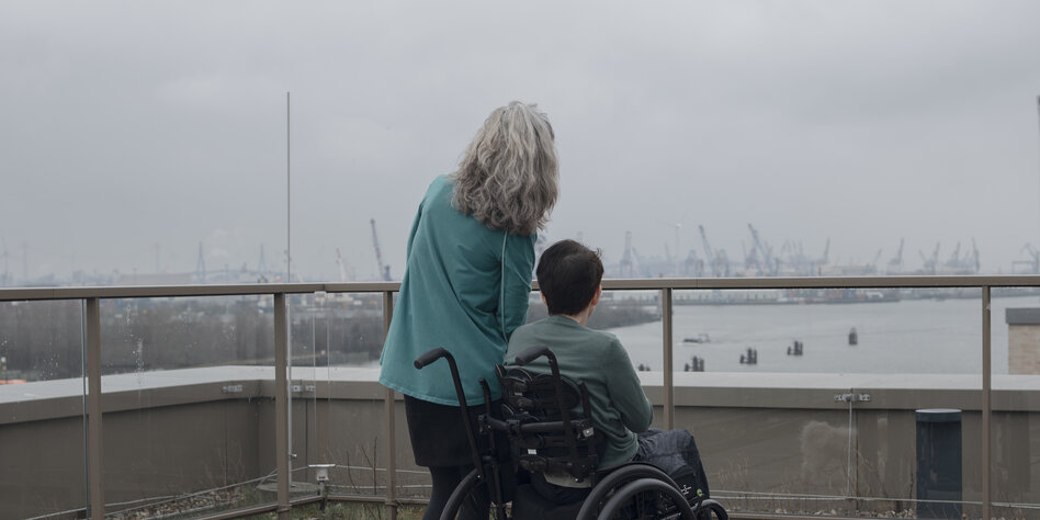 Zwei Frauen, eine davon im Rollstuhl, blicken vom Dach eines Hauses auf die Elbe