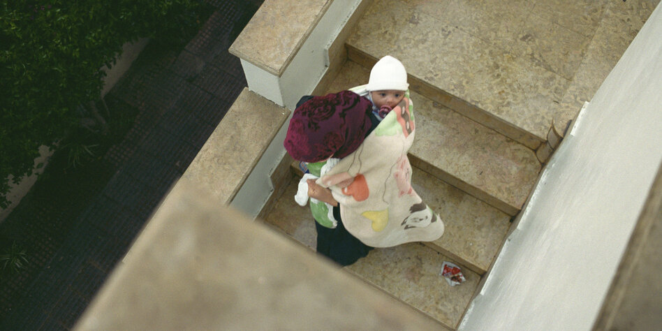 Eine Frau hat mit einer Decke ein Baby auf den Rücken gespannt und geht eine Treppe herunter