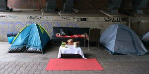 Zelte und ein gedeckter Tisch mit Kuschelbär unter einer S-Bahn Brücke