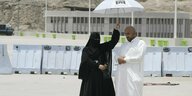 In Mekka hält eine verschleierte Frau einen Sonnenschirm über einen Mann, der sein Gebet verrichtet.