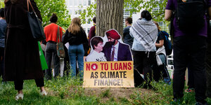 Ein Plakat auf dem steht "Keine Kredite für Klimafinanzierung" lehnt an einem Baum