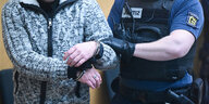 Ein Polizist führt einen Mann mit Handschellen in einen Gerichtssaal (Detailaufnahme)