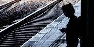 Eine Frau steht am Berliner Bahnhof Ostkreuz am Bahnsteig und schaut auf das Handy.