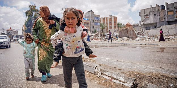 Ein Mädchen trägt ihre kleine Schwester auf dem Rücken und flieht mit ihrer Familie vor der Israelischen Offensive aus Rafah