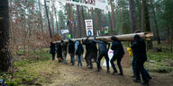 ktivisten tragen in einem Protestcamp einen Baumstamm im Wald. Das Protestcamp richtet sich gegen eine geplante Erweiterung des Tesla-Werksgeländes in einem Waldgebiet nahe der Fabrik.