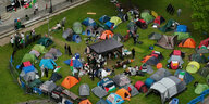 Auf einer Wiese stehen Zelte, dazwischen hängen Transparente, unter anderem: "End Genocide"